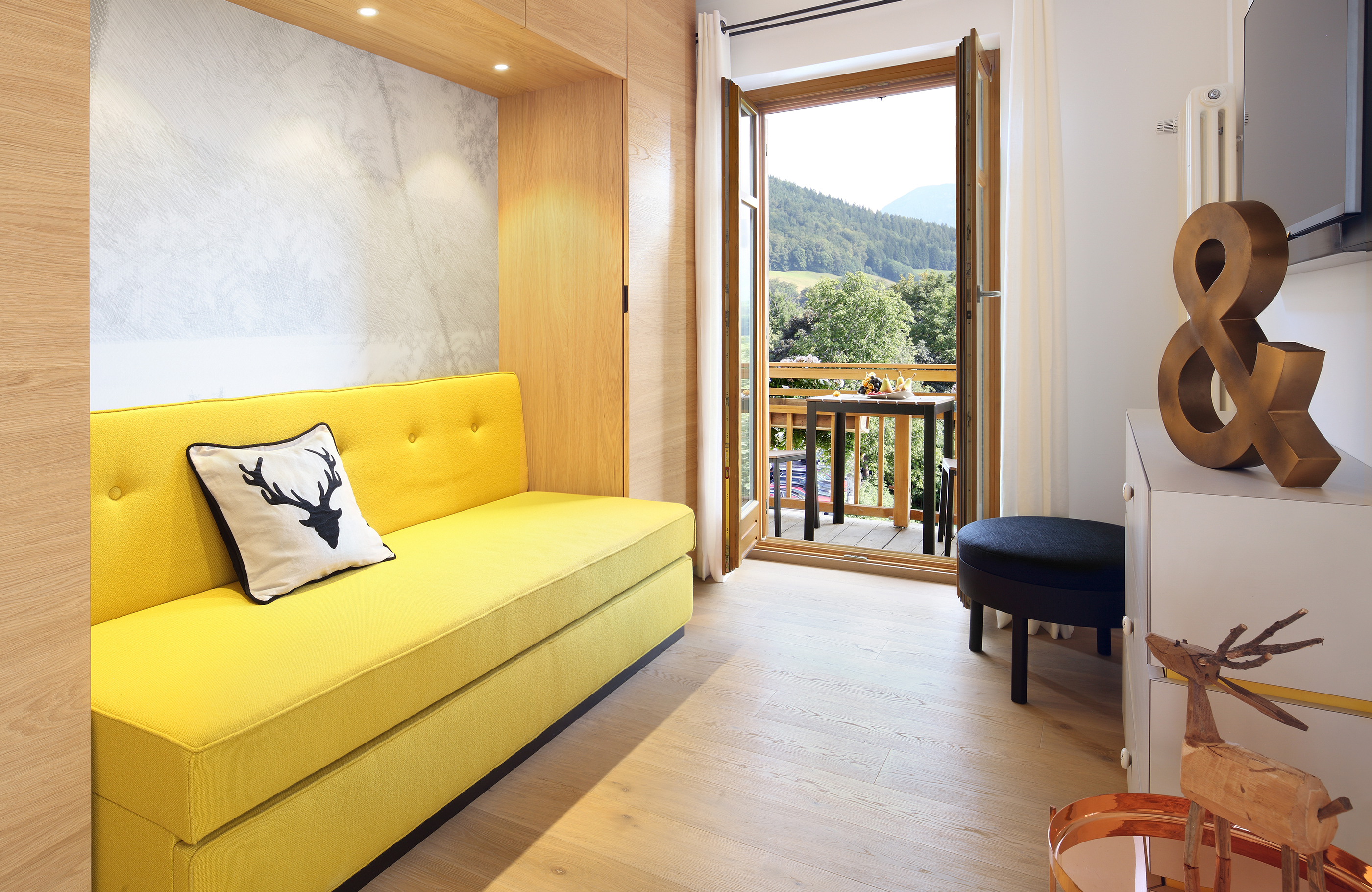 Ein gelbes Sofa steht vor einer Balkontür und einem TV in einer Suite des Hotels