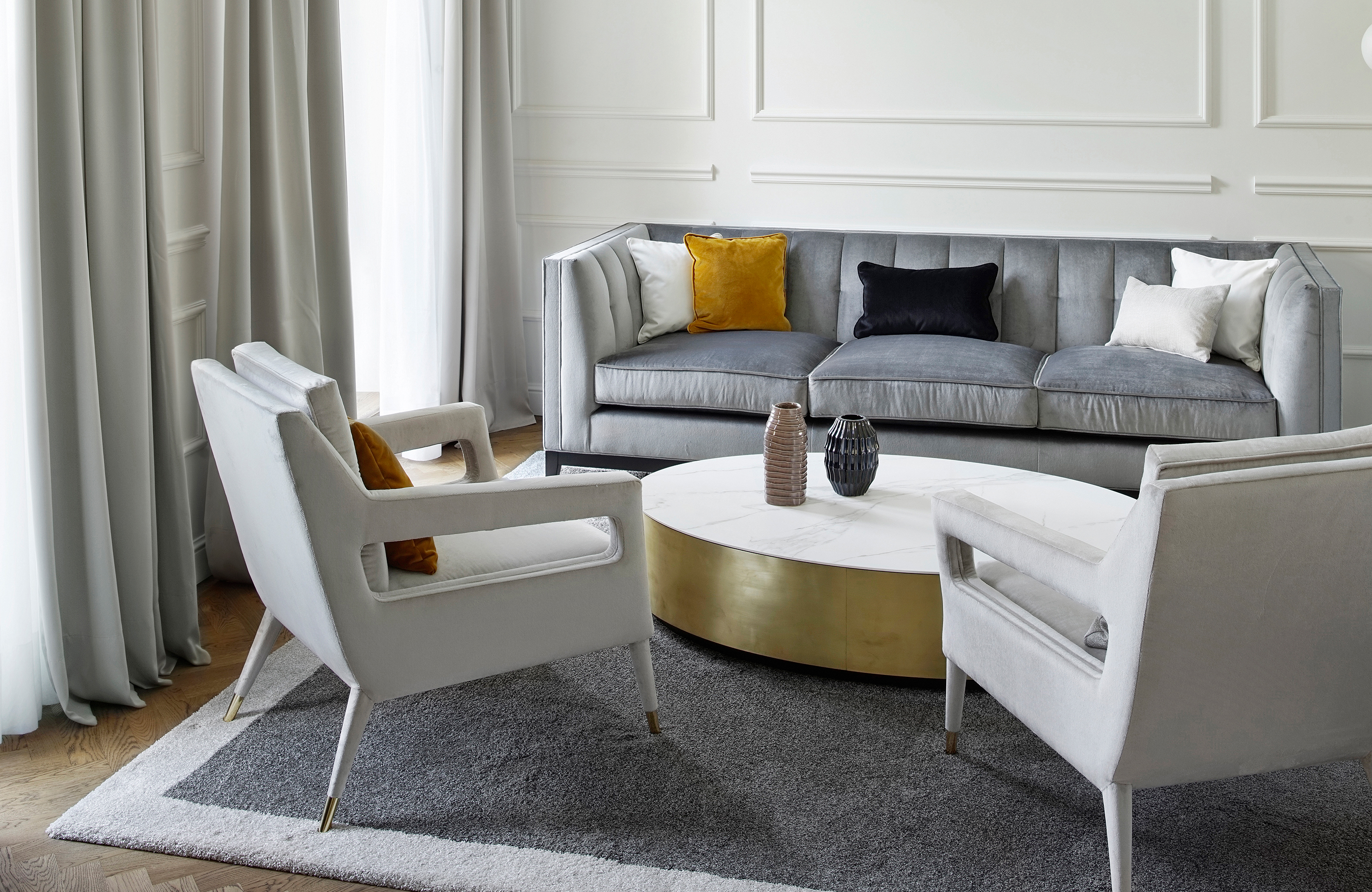 Aufnahme des Wohnzimmers mit einer grauen Couch aus Samt und zwei hellen Sesseln