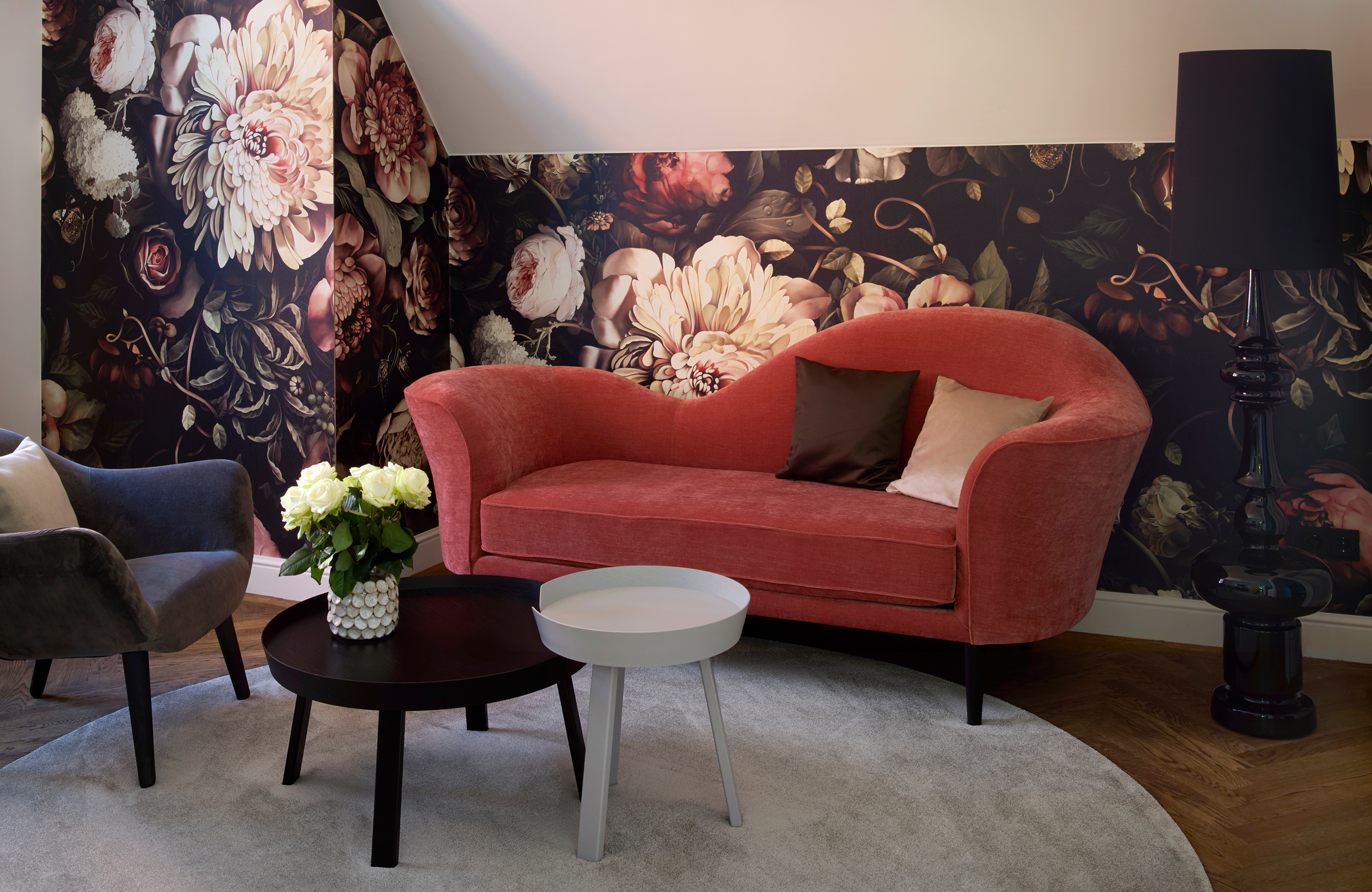 Blick auf ein rotes geschwungenes Sofa vor einer Wand mit Blumentapete