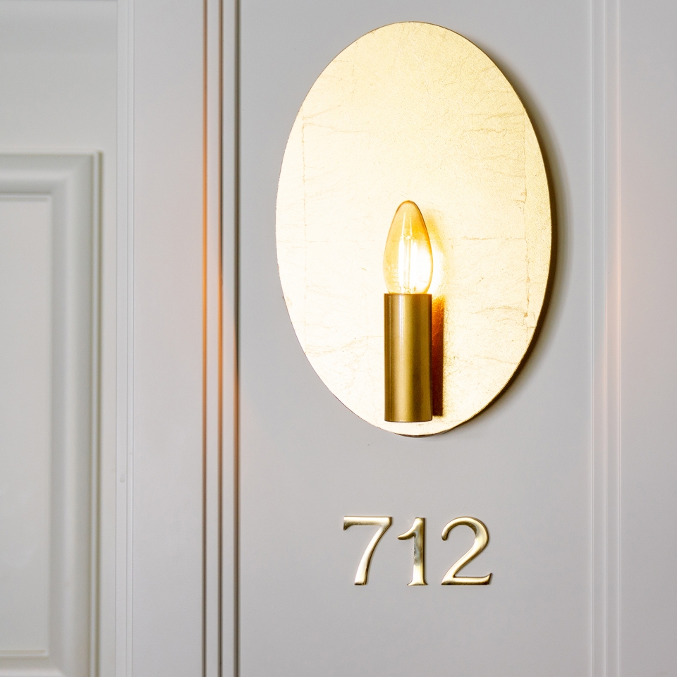 Nahaufnahme einer Zimmernummer die unter einer goldenen Wandlampe hängt