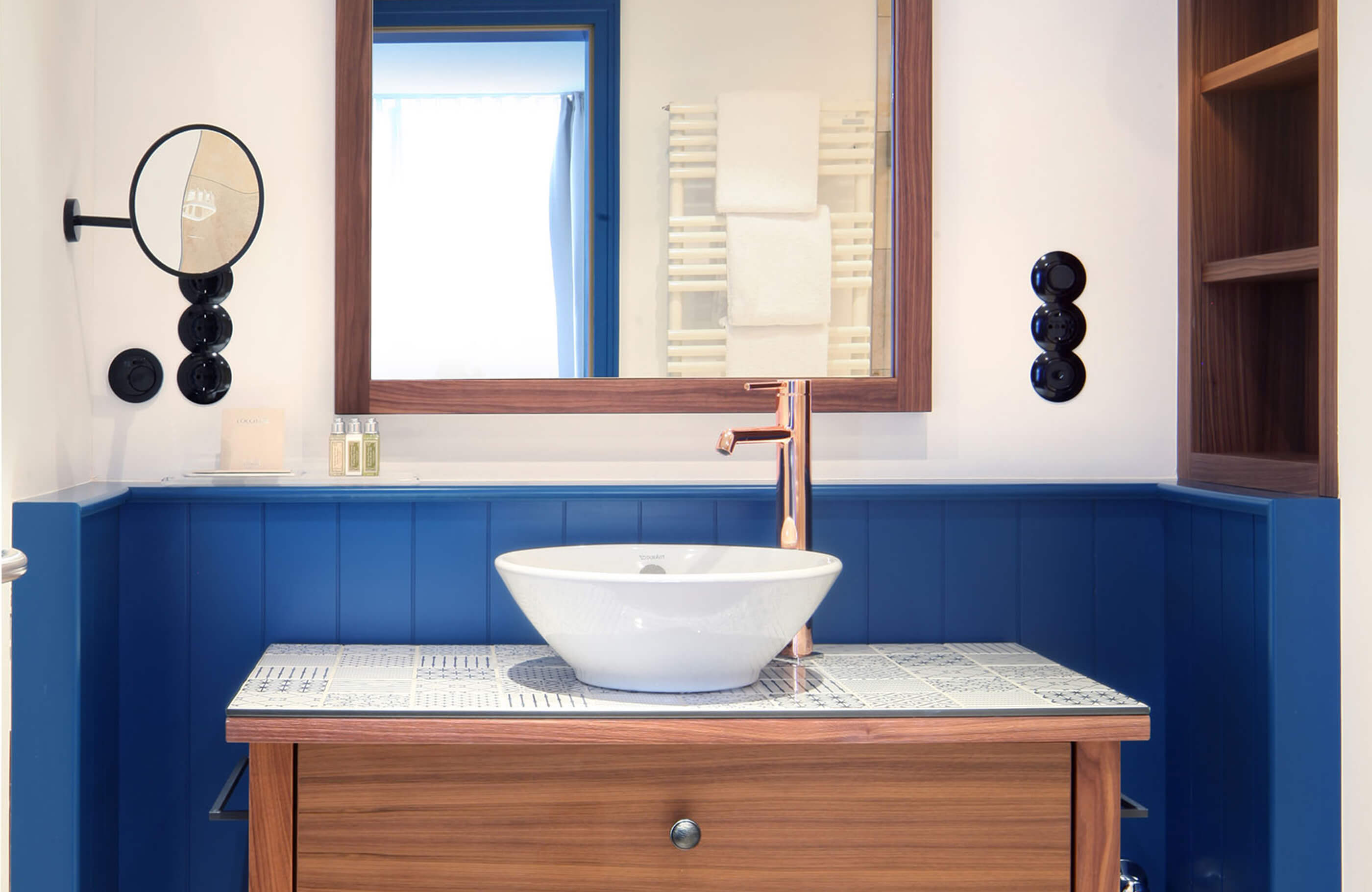 Aufnahme im Badezimmer des Herberge Quirin im Hotel Das Tegernsee mit einem freistehenden, weißen Waschbecken, einem kupferfarbenem Wasserhahn und einem Wandspiegel.