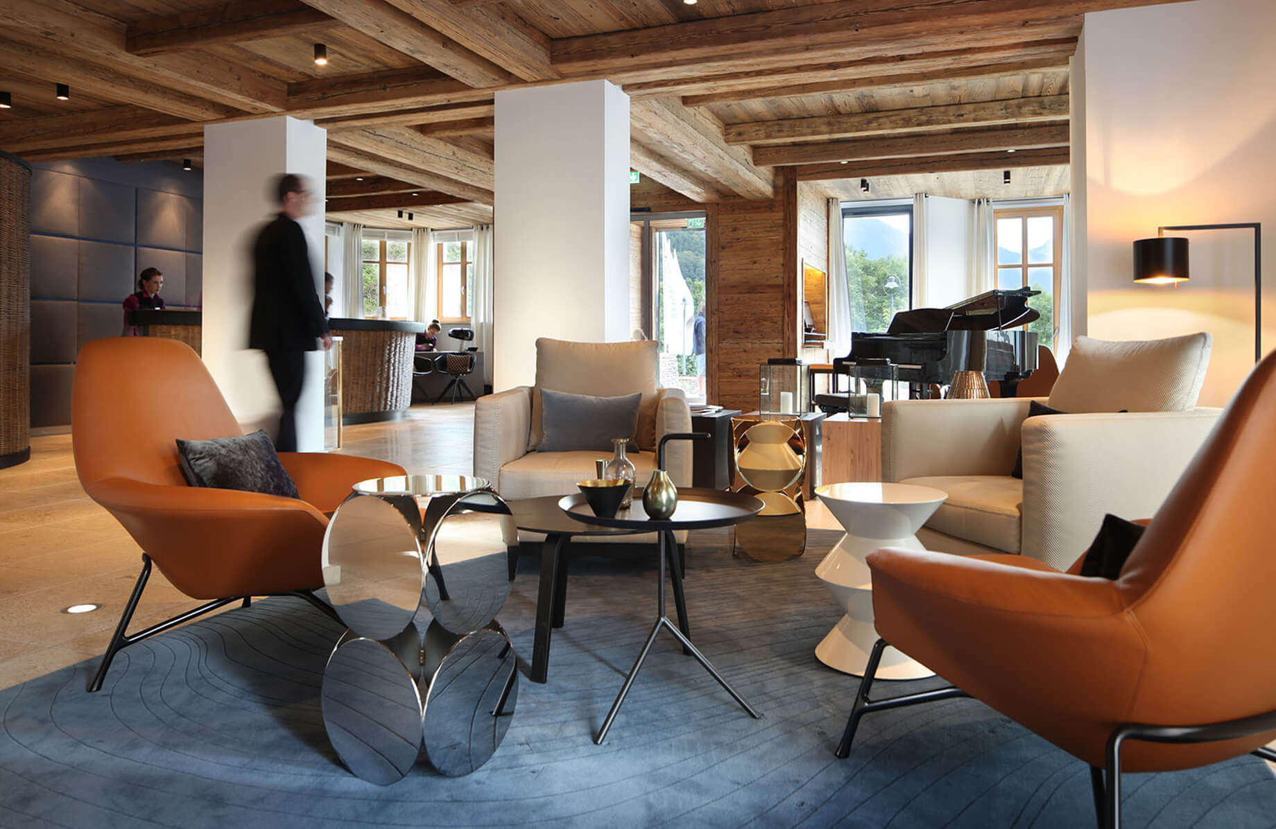 Aufnahme in der hellen Lobby des Hotels Das Tegernsee, die modern und gemütlich eingerichtet ist mit zwei braunen Lounge-Stühlen und zwei grauen Ledersesseln in der Raummitte.