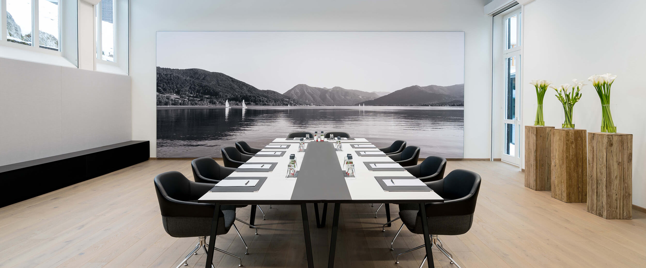 Blick in einen Tagungsraum im Hotel Das Tegernsee mit einem langen, weißen Konferenztisch und schwarzen modernen Armlehnen-Stühlen für korporative Veranstaltungen am Tegernsee