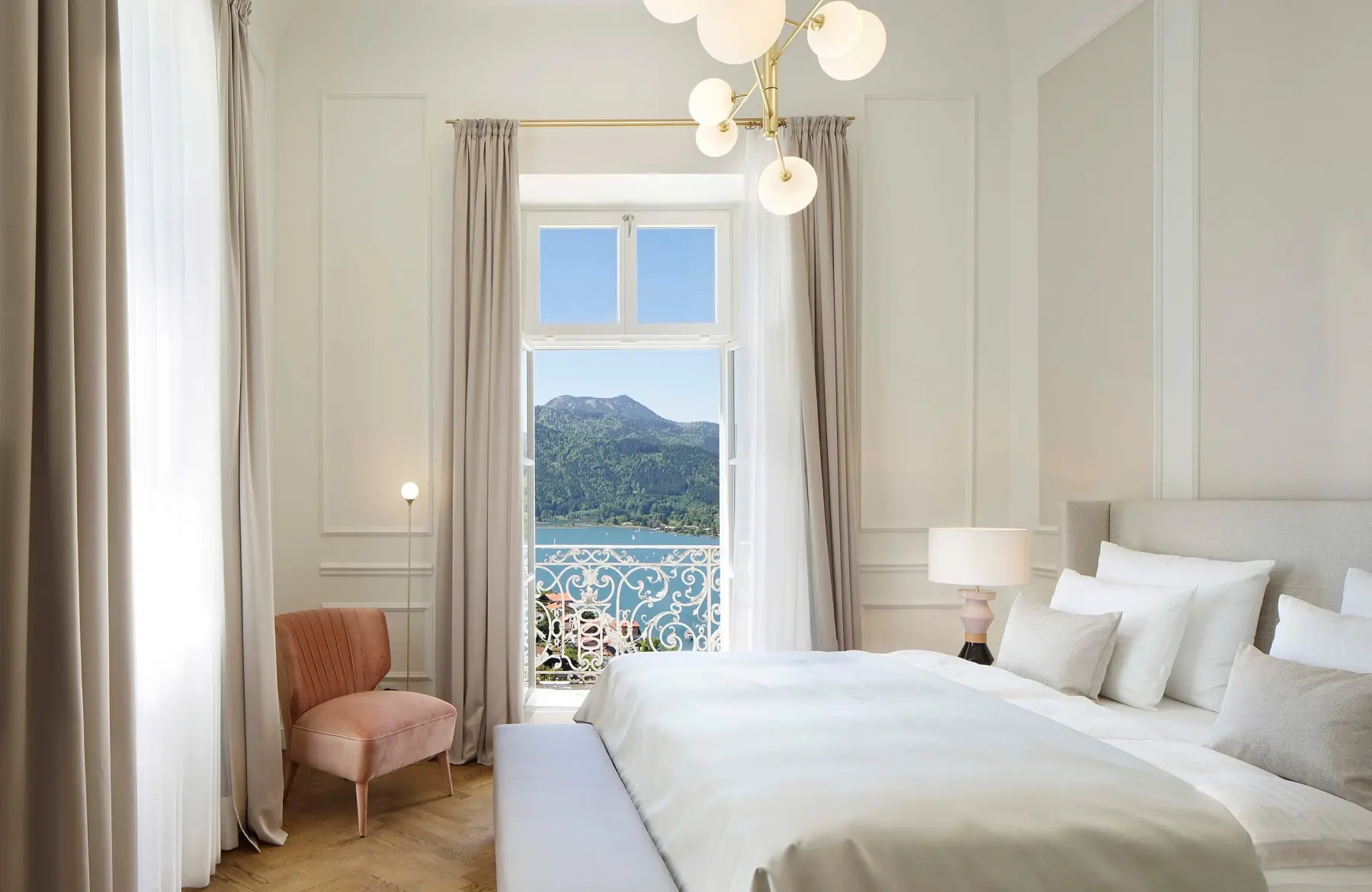 Doppelbett neben einem Fenster mit Blick auf den Tegernsee im Lifestyle Hotel in Bayern