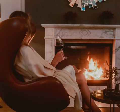 Frau sitzt mit Weinglas in der Hand am Kaminfeuer