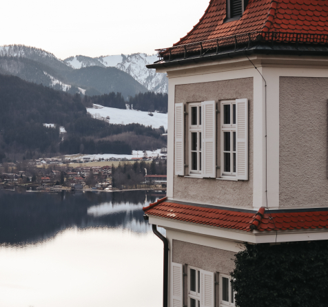 Panoramablick auf den Tegernsee mit schneebedeckten Gipfeln und dem Sengerschloss Gebäude auf der rechten Seite