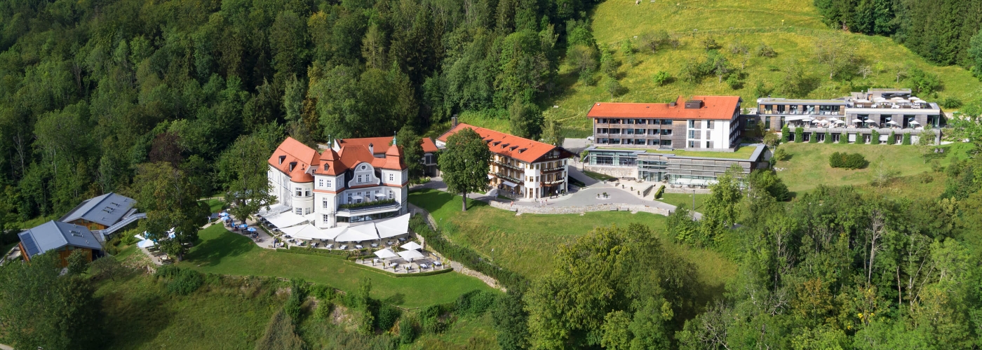 Aufnahme von der Anlage des Hotels Das Tegernsee mit seinen fünf Häusern, die sich inmitten einer Grünfläche befinden und namentlich gekennzeichnet sind.