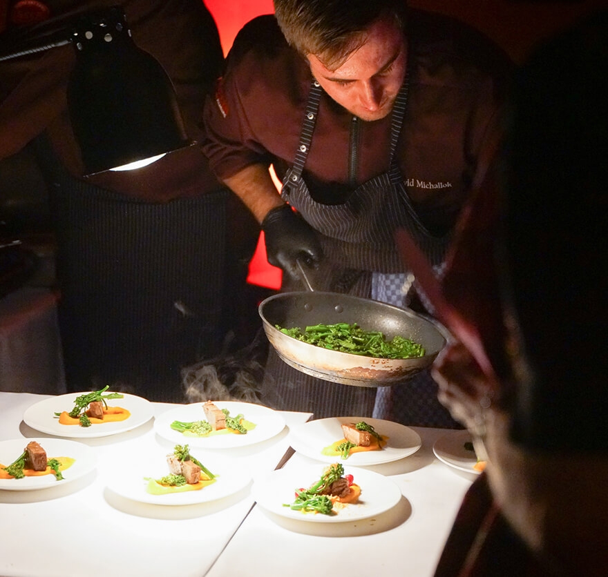 Bild von einem Koch im Hotel Das Tegernsee, der gerade frisches Gemüse aus einer Pfanne während einem Event mit Live-Cooking auf einem Tellergericht anrichtet.