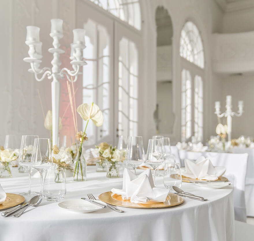 Detailaufnahme von mehreren in weiß-goldenen Farben festlich eingedeckten Rundtischen im Barocksaal des Hotels Das Tegernsee.
