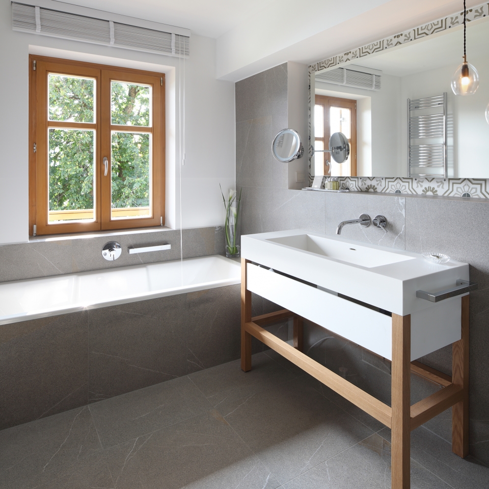 Großzügiges graues Badezimmer mit hellem Fenster und Badewanne
