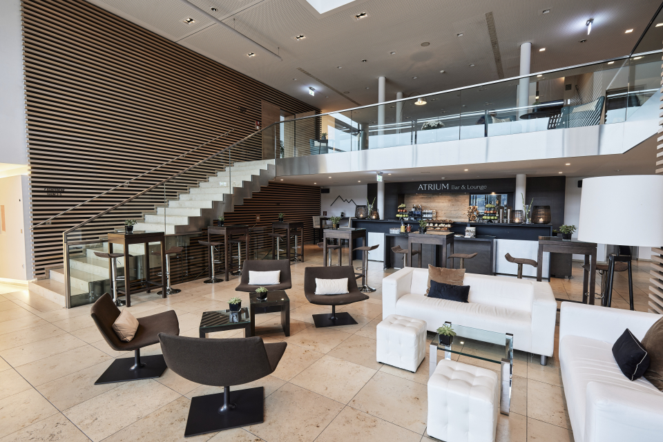 Atrium-Foyer mit Loungemöbeln, offener Treppe und Kaffeebar
