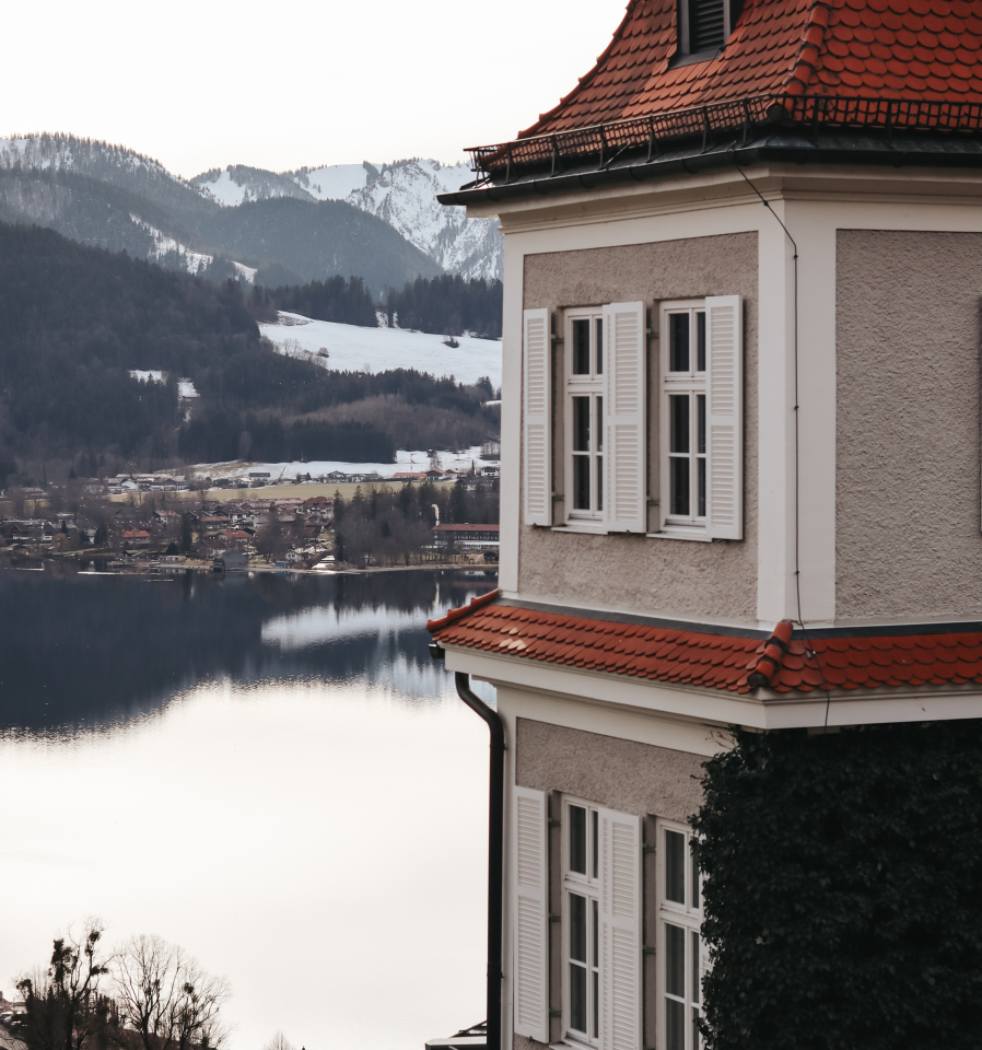 Panoramablick auf den Tegernsee mit schneebedeckten Gipfeln und dem Sengerschloss Gebäude auf der rechten Seite